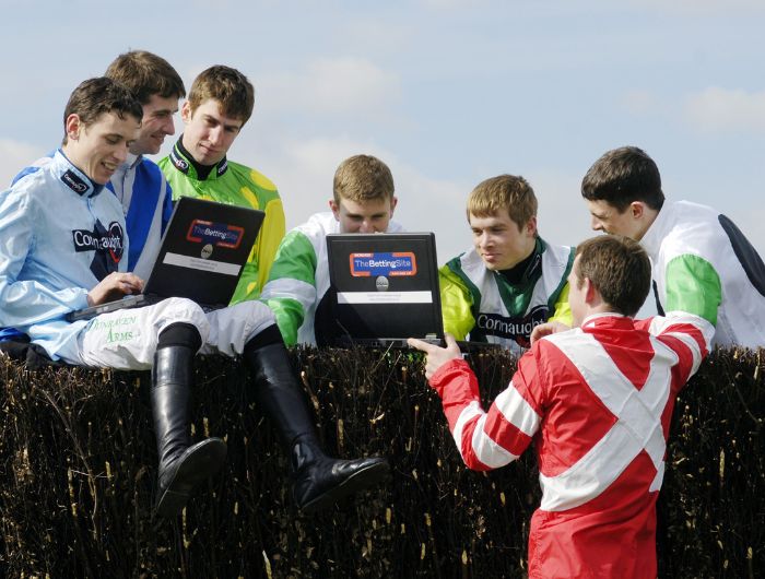 Jockeys sit around hurdle and look at a laptop