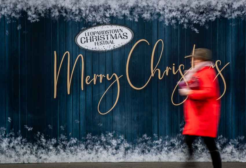 A lady walking past a Merry Christmas sign at The Leopardstown Christmas Festival